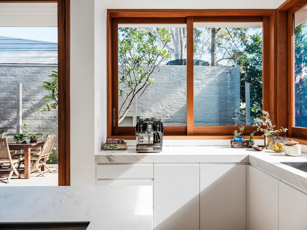 Inspiration for a large contemporary galley eat-in kitchen in Sydney with a drop-in sink, flat-panel cabinets, white cabinets, quartz benchtops, metallic splashback, metal splashback, stainless steel appliances, concrete floors, with island, grey floor and white benchtop.
