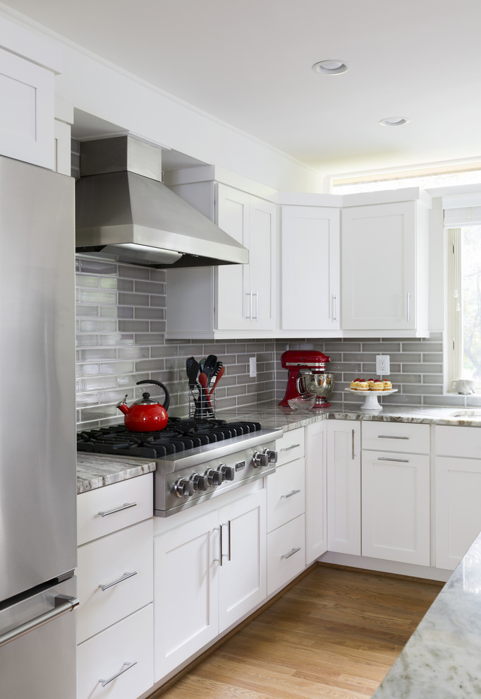 Inspiration for a large transitional l-shaped separate kitchen in DC Metro with an undermount sink, shaker cabinets, white cabinets, marble benchtops, grey splashback, ceramic splashback, stainless steel appliances, light hardwood floors, with island and brown floor.