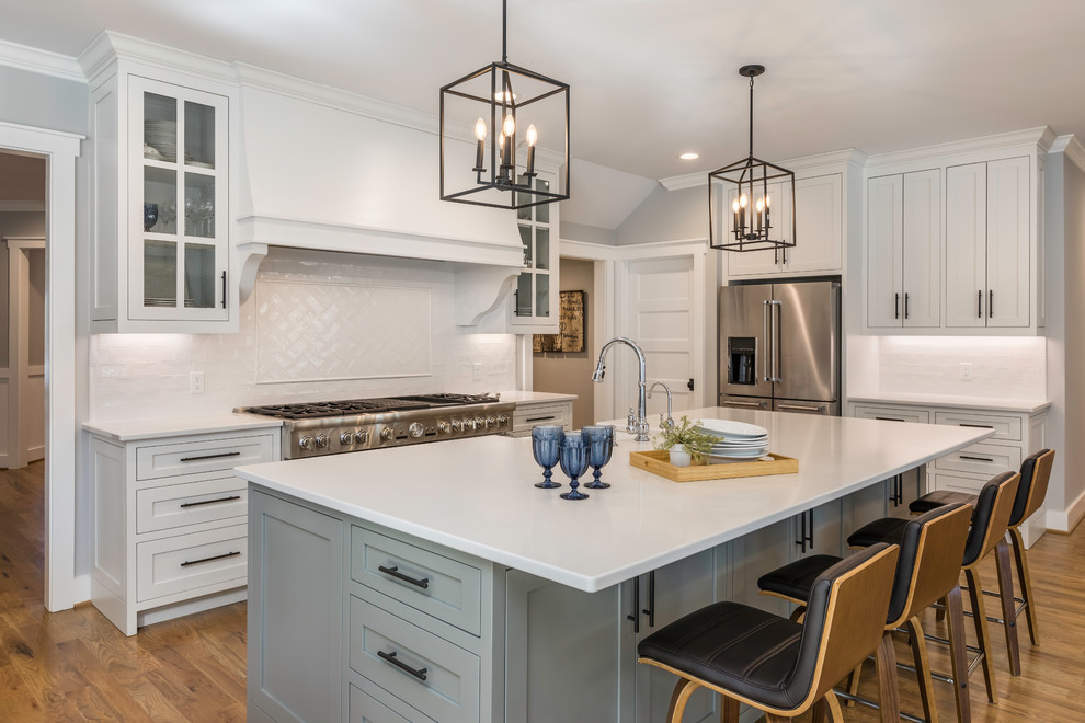 Design ideas for a large country l-shaped eat-in kitchen in Other with a farmhouse sink, grey cabinets, quartzite benchtops, white splashback, ceramic splashback, stainless steel appliances, medium hardwood floors, with island, brown floor, white benchtop and shaker cabinets.