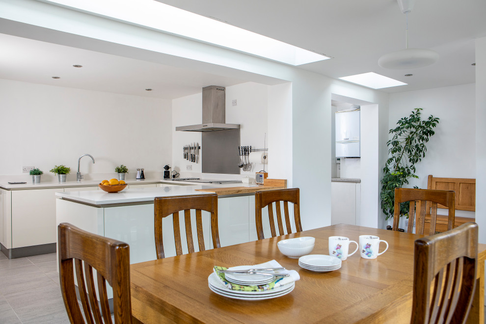 Design ideas for a mid-sized contemporary u-shaped eat-in kitchen in Other with an undermount sink, flat-panel cabinets, white cabinets, solid surface benchtops, metallic splashback, metal splashback, panelled appliances, ceramic floors, no island, grey floor and white benchtop.