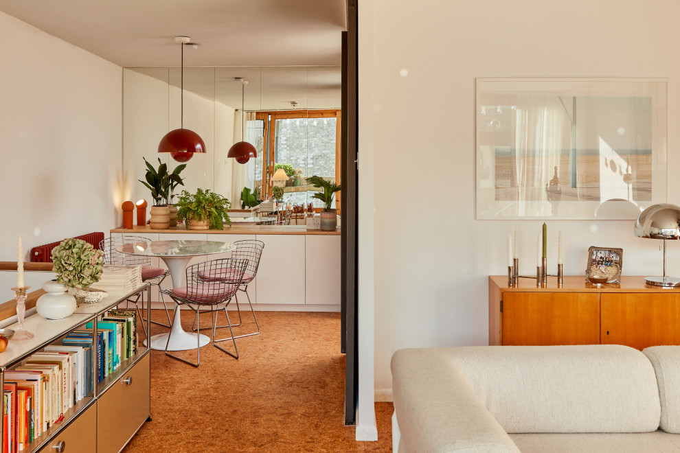 This is an example of a midcentury dining room in Berlin with white walls, orange floor and cork floors.