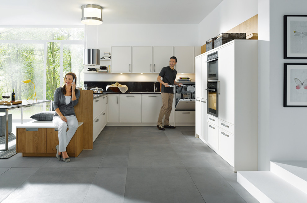 Photo of a medium sized modern u-shaped kitchen/diner in Surrey with shaker cabinets, white cabinets, granite worktops, black splashback, stone slab splashback, stainless steel appliances and a breakfast bar.
