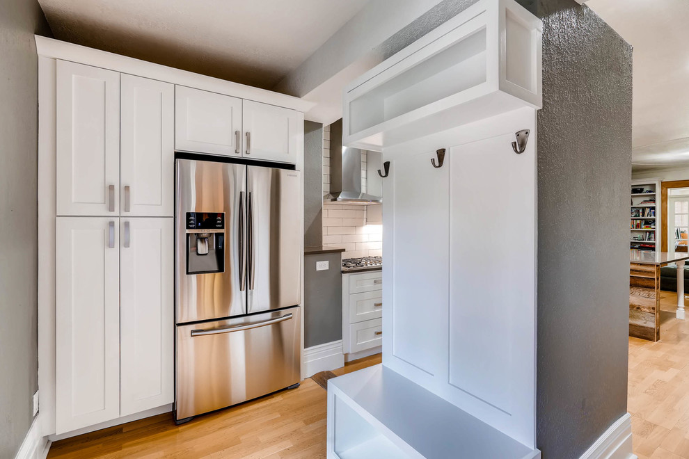 Inspiration for a large rustic light wood floor and brown floor eat-in kitchen remodel in Denver with a farmhouse sink, shaker cabinets, white cabinets, quartz countertops, white backsplash, ceramic backsplash, stainless steel appliances, a peninsula and brown countertops