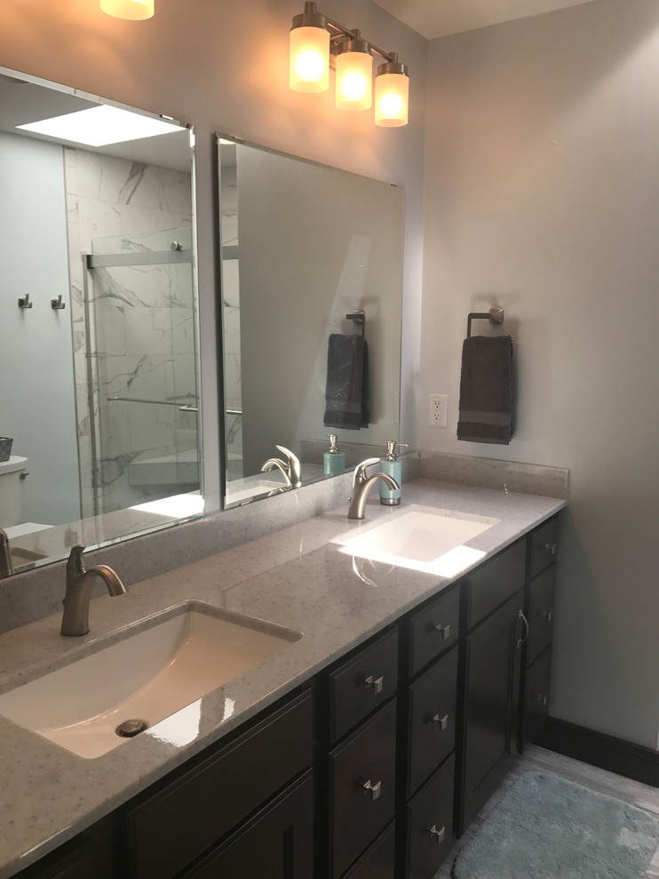 Inspiration for a mid-sized transitional master bathroom in Milwaukee with flat-panel cabinets, dark wood cabinets, an alcove shower, a two-piece toilet, white tile, porcelain tile, grey walls, laminate floors, an integrated sink, solid surface benchtops, grey floor and a sliding shower screen.