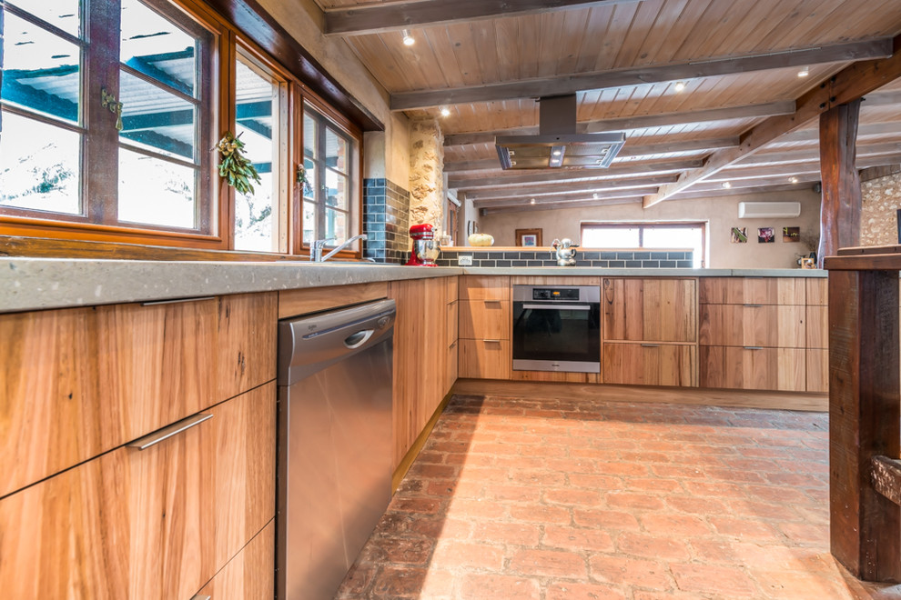 Mid-sized country l-shaped eat-in kitchen in Adelaide with a double-bowl sink, flat-panel cabinets, medium wood cabinets, concrete benchtops, black splashback, subway tile splashback, stainless steel appliances, brick floors and with island.