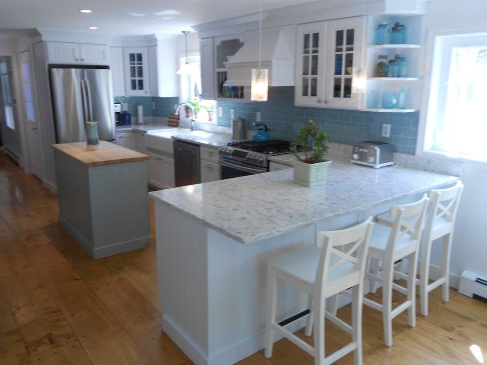 Inspiration for a large beach style u-shaped eat-in kitchen in Portland Maine with a farmhouse sink, louvered cabinets, white cabinets, marble benchtops, blue splashback, subway tile splashback, stainless steel appliances, medium hardwood floors and with island.