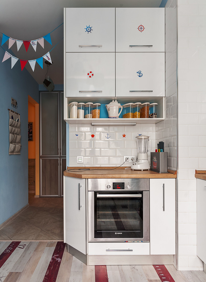 This is an example of a small beach style l-shaped separate kitchen in Moscow with flat-panel cabinets, white cabinets, white splashback, subway tile splashback, stainless steel appliances, wood benchtops and painted wood floors.