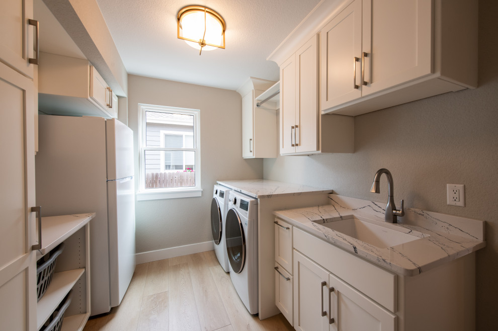 Photo of a small modern galley utility room in Other with a drop-in sink, marble benchtops, grey walls, light hardwood floors, a side-by-side washer and dryer and multi-coloured benchtop.