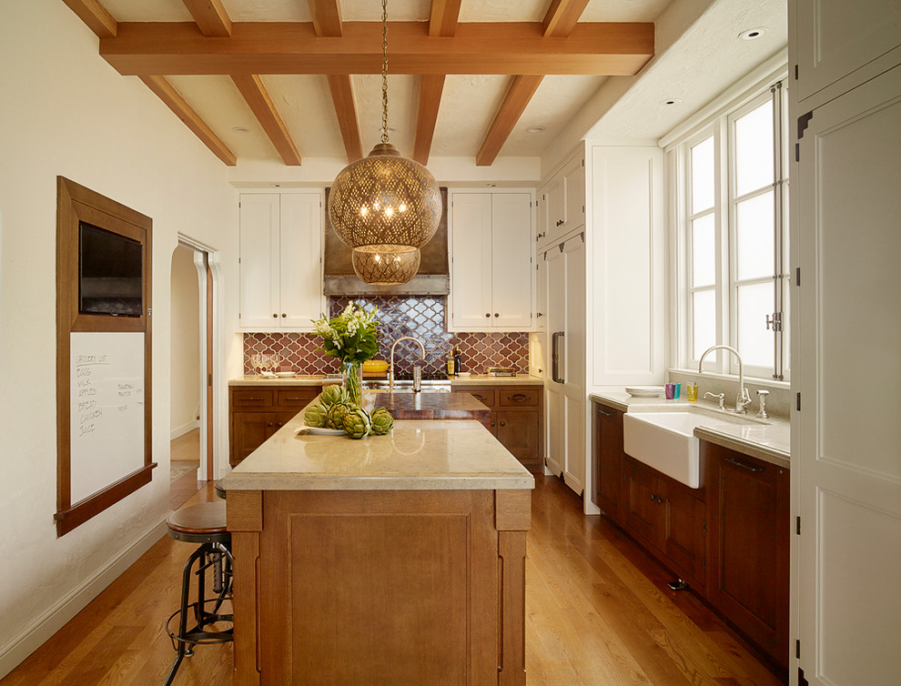 This is an example of a large mediterranean l-shaped separate kitchen in San Francisco with a farmhouse sink, beaded inset cabinets, white cabinets, limestone benchtops, panelled appliances, medium hardwood floors, with island, brown splashback and brown floor.