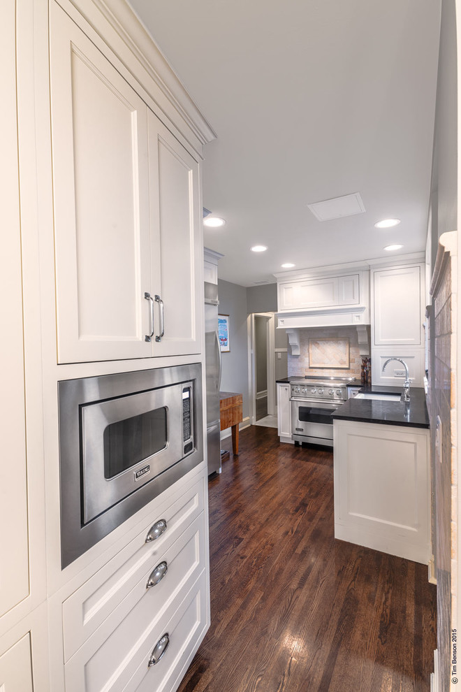 Inspiration for a small transitional galley separate kitchen in Chicago with a farmhouse sink, shaker cabinets, white cabinets, granite benchtops, beige splashback, stone tile splashback, stainless steel appliances, dark hardwood floors and no island.