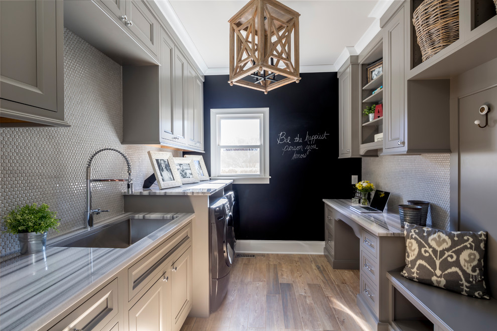 Design ideas for a mid-sized transitional galley utility room in Charlotte with an undermount sink, recessed-panel cabinets, grey cabinets, marble benchtops, dark hardwood floors, a side-by-side washer and dryer and black walls.
