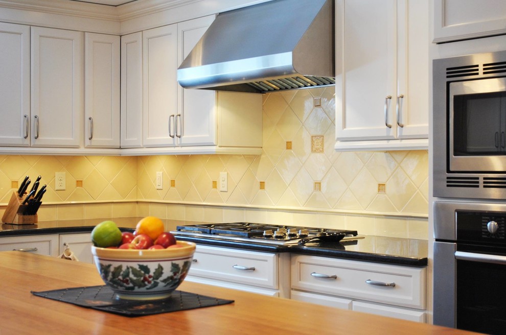 Inspiration for a mid-sized transitional l-shaped kitchen remodel in Boston with recessed-panel cabinets, white cabinets, beige backsplash, ceramic backsplash, stainless steel appliances and an island