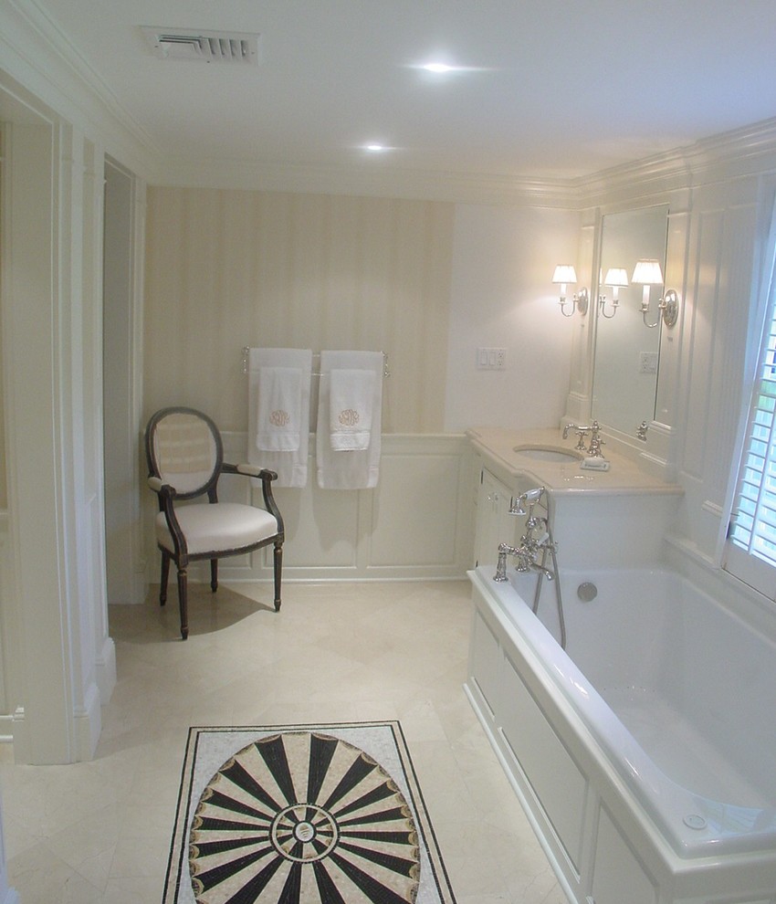 This is an example of a traditional master bathroom in New York with a drop-in tub, white tile, beige walls, an undermount sink, raised-panel cabinets, white cabinets, marble benchtops, an alcove shower, a two-piece toilet, stone tile and mosaic tile floors.