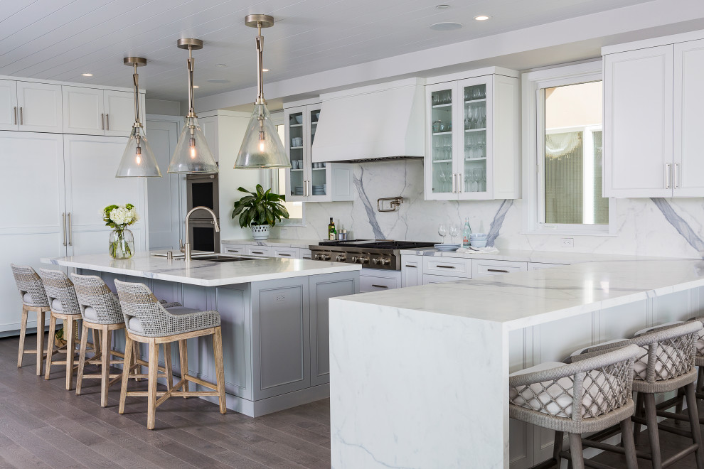 This is an example of a large coastal u-shaped open plan kitchen in Los Angeles with shaker cabinets, white cabinets, engineered stone countertops, white splashback, an island and white worktops.