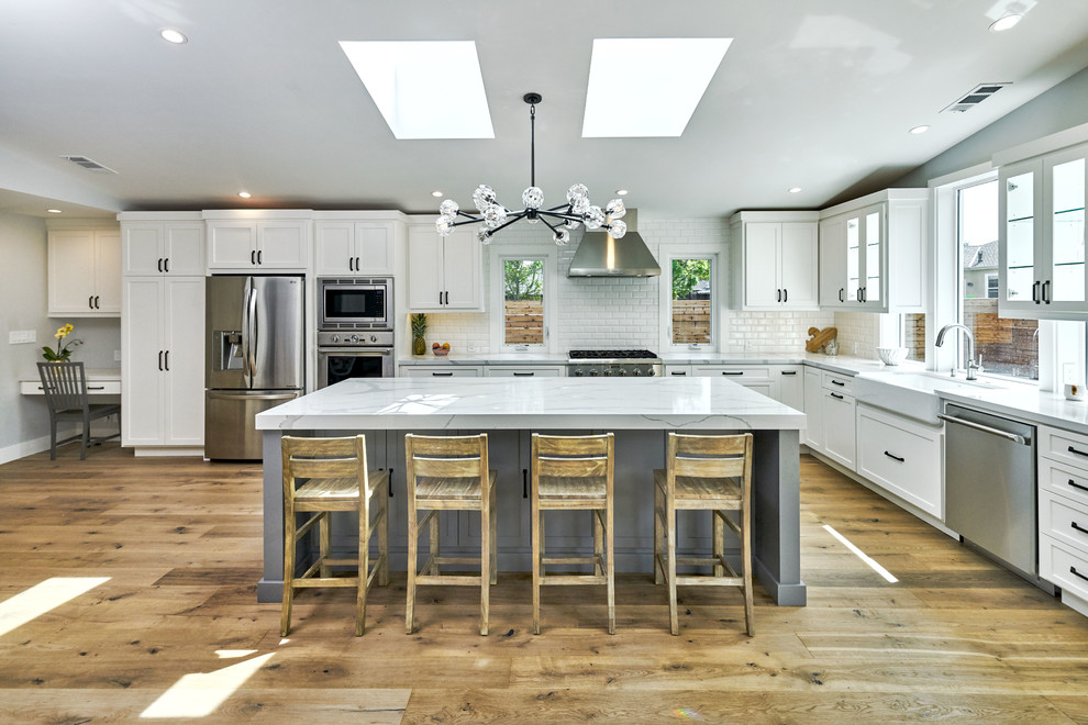Inspiration for a country l-shaped kitchen in San Francisco with a farmhouse sink, shaker cabinets, white cabinets, white splashback, subway tile splashback, stainless steel appliances, medium hardwood floors and with island.