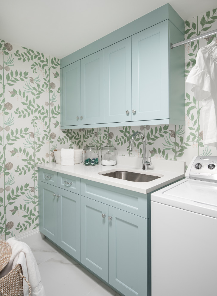 Mid-sized beach style single-wall dedicated laundry room in Other with an undermount sink, shaker cabinets, blue cabinets, quartz benchtops, engineered quartz splashback, porcelain floors, a side-by-side washer and dryer, white floor, white benchtop and wallpaper.