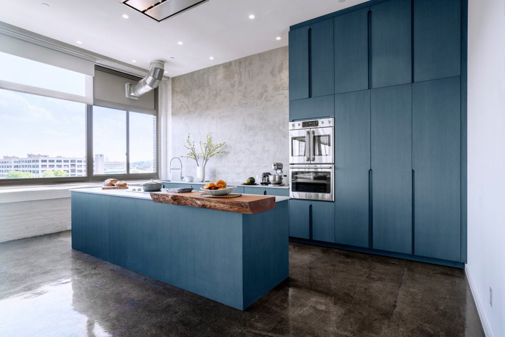 Large contemporary single-wall open plan kitchen in New York with a farmhouse sink, flat-panel cabinets, blue cabinets, quartz benchtops, grey splashback, cement tile splashback, stainless steel appliances, cement tiles, with island, black floor and grey benchtop.