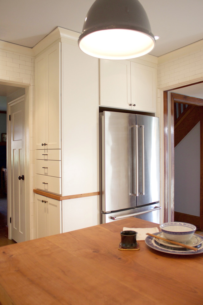 Inspiration for a mid-sized transitional kitchen remodel with glass-front cabinets, white cabinets, wood countertops, white backsplash, subway tile backsplash, stainless steel appliances and an island
