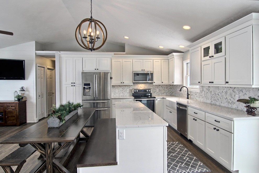 Example of a mid-sized transitional l-shaped vinyl floor eat-in kitchen design with a farmhouse sink, shaker cabinets, white cabinets, quartz countertops, white backsplash, stone tile backsplash, stainless steel appliances and an island