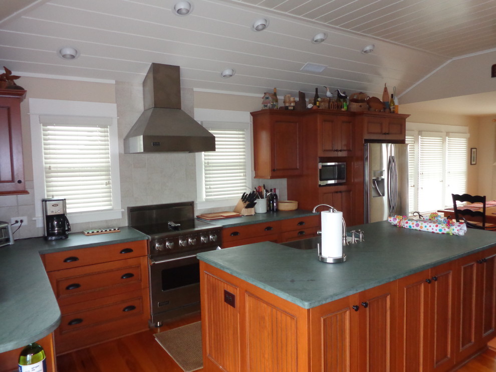 This is an example of a mid-sized beach style l-shaped eat-in kitchen in Other with a farmhouse sink, recessed-panel cabinets, blue cabinets, soapstone benchtops, beige splashback, ceramic splashback, stainless steel appliances, dark hardwood floors, with island and turquoise benchtop.