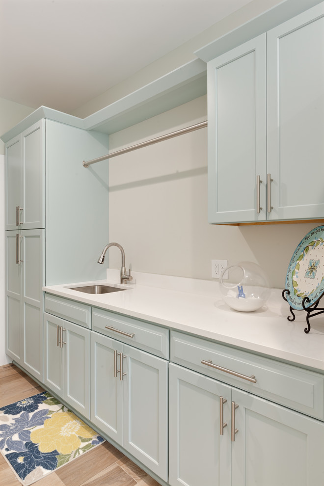 Large contemporary l-shaped dedicated laundry room in Atlanta with an undermount sink, shaker cabinets, quartz benchtops, porcelain floors, a stacked washer and dryer, blue cabinets, white walls, beige floor and white benchtop.