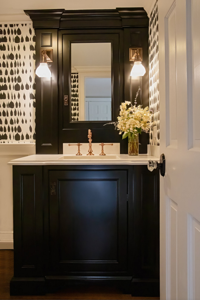 Inspiration for a small beach style powder room in Bridgeport with recessed-panel cabinets, black cabinets, a two-piece toilet, black walls, medium hardwood floors, an undermount sink, solid surface benchtops, brown floor, white benchtops, a built-in vanity and wallpaper.