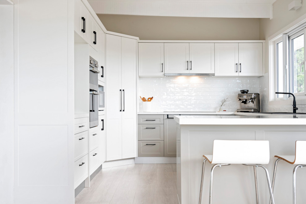 Design ideas for a medium sized contemporary u-shaped kitchen pantry in Sydney with shaker cabinets, white cabinets, engineered stone countertops, white splashback, ceramic splashback, stainless steel appliances, a breakfast bar and white worktops.
