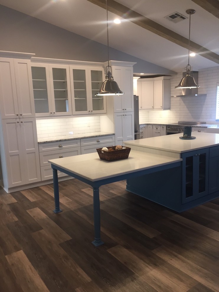 Large beach style l-shaped eat-in kitchen in Tampa with a farmhouse sink, shaker cabinets, white cabinets, granite benchtops, white splashback, subway tile splashback, stainless steel appliances, vinyl floors, with island and grey floor.
