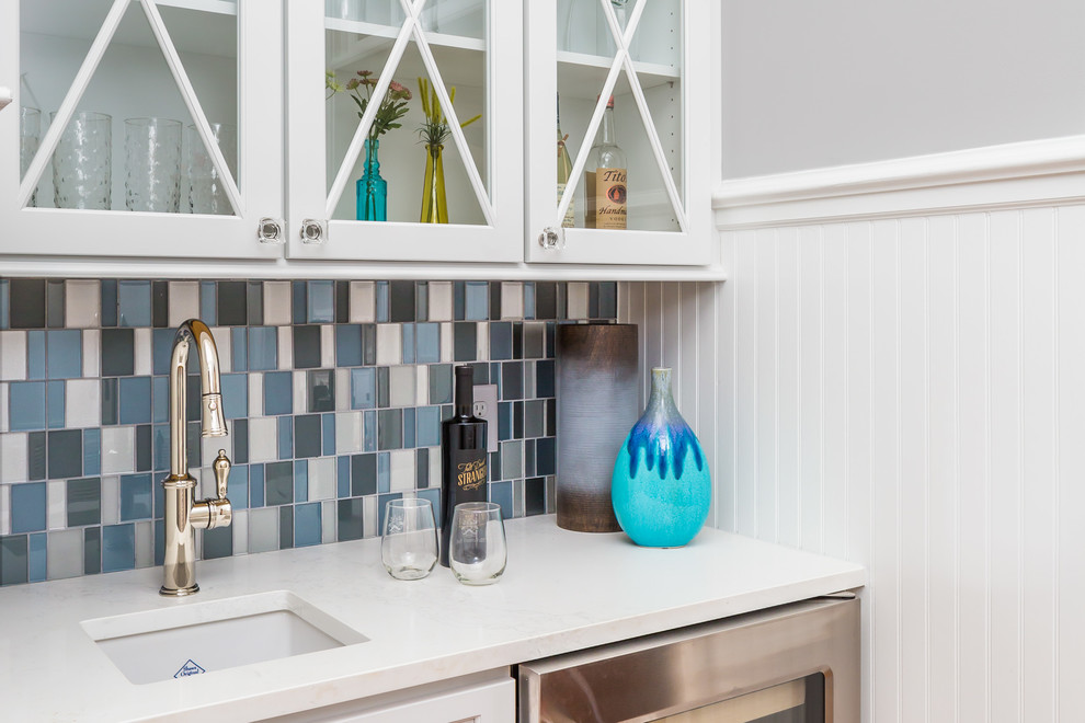 Example of a large transitional l-shaped medium tone wood floor open concept kitchen design in Raleigh with a farmhouse sink, flat-panel cabinets, white cabinets, quartz countertops, blue backsplash, glass tile backsplash, stainless steel appliances and an island