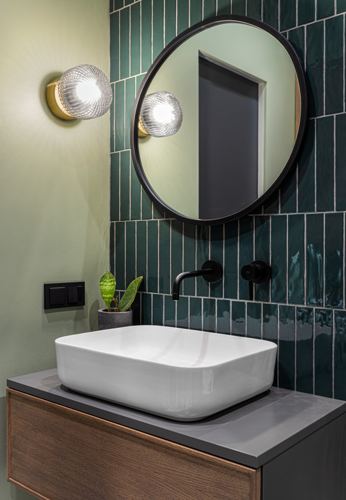 Photo of a small cloakroom in Moscow with raised-panel cabinets, dark wood cabinets, a wall mounted toilet, green tiles, ceramic tiles, green walls, a built-in sink, solid surface worktops, white floors, grey worktops, feature lighting and a floating vanity unit.