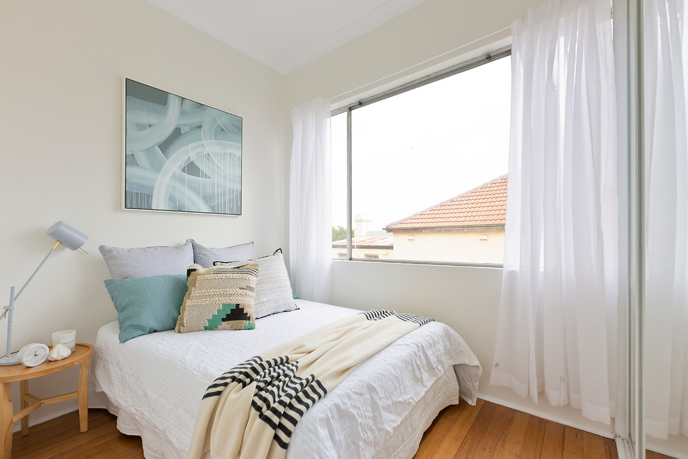 Design ideas for a mid-sized transitional guest bedroom in Sydney with medium hardwood floors, beige walls and brown floor.