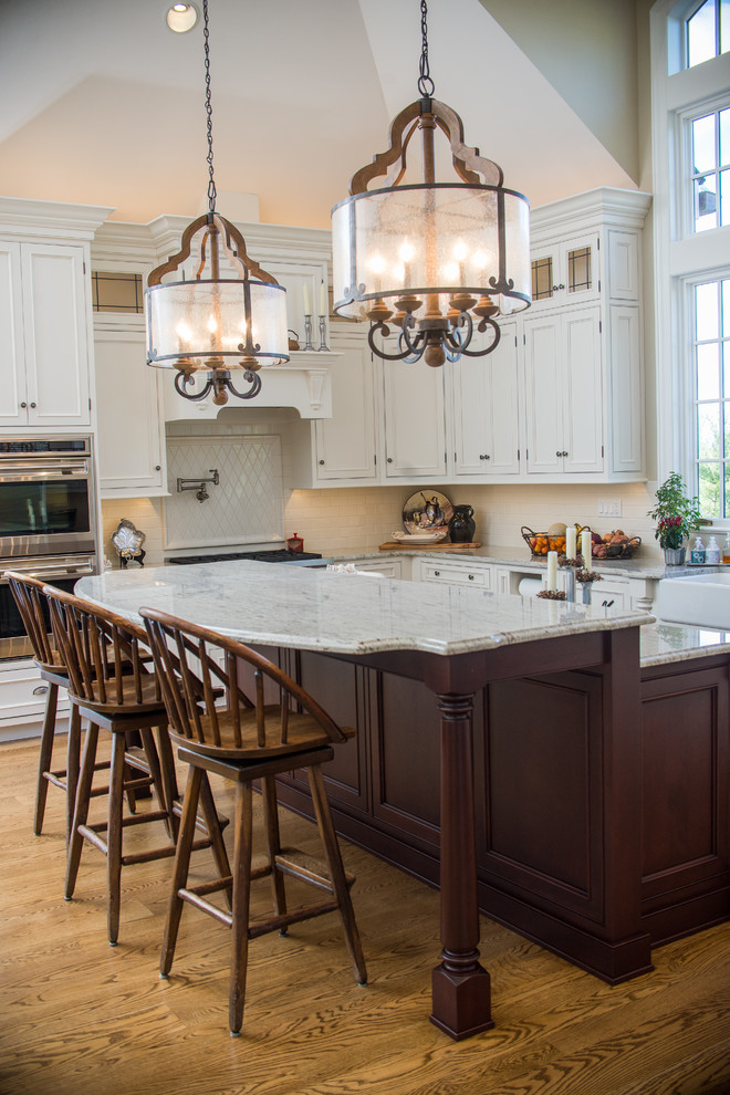 Photo of a mid-sized traditional u-shaped eat-in kitchen in Baltimore with a farmhouse sink, glass-front cabinets, white cabinets, white splashback, stainless steel appliances and with island.