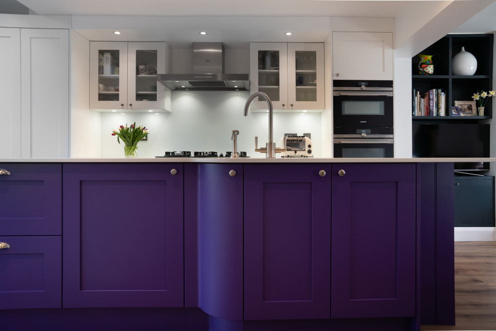 Inspiration for a large traditional single-wall open plan kitchen in London with an integrated sink, purple cabinets, solid surface benchtops, white splashback, glass sheet splashback, stainless steel appliances, dark hardwood floors, with island and white benchtop.