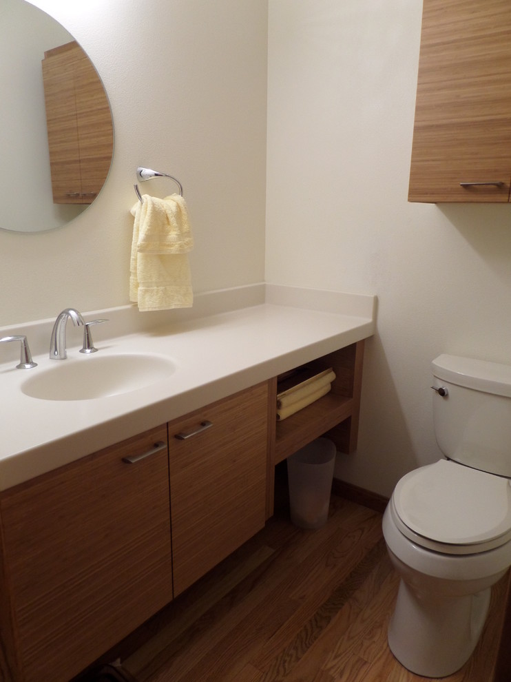 Inspiration for a small modern 3/4 bathroom in Cedar Rapids with an integrated sink, flat-panel cabinets, medium wood cabinets, solid surface benchtops, a two-piece toilet and light hardwood floors.
