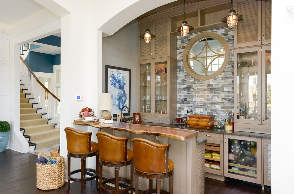 Beach style seated home bar in Other with glass-front cabinets, brown cabinets, multi-coloured splashback, dark hardwood floors and brown floor.