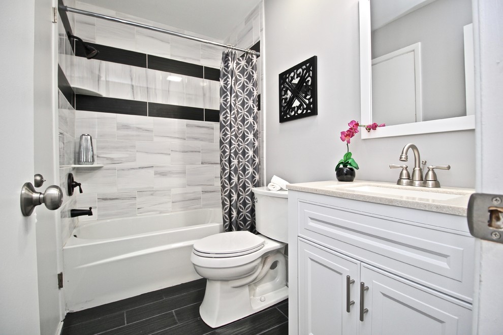 Photo of a small contemporary bathroom in Philadelphia with raised-panel cabinets, white cabinets, an alcove tub, a shower/bathtub combo, a two-piece toilet, multi-coloured tile, ceramic tile, grey walls, ceramic floors, a console sink, marble benchtops, brown floor, a shower curtain and beige benchtops.