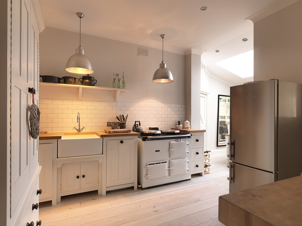 Design ideas for a mid-sized scandinavian kitchen in London with a farmhouse sink, shaker cabinets, white cabinets, white splashback, subway tile splashback, stainless steel appliances, light hardwood floors, no island and beige floor.