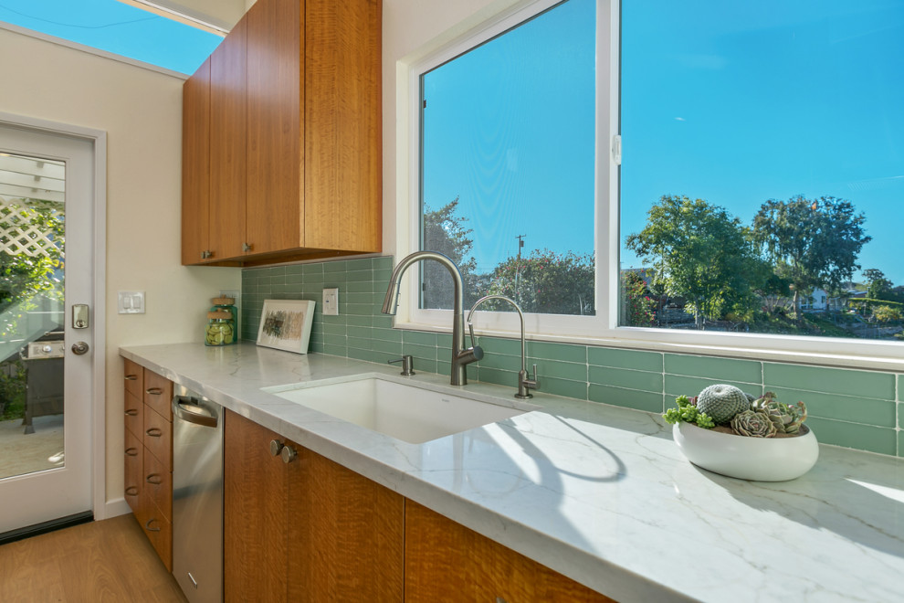 Photo of a mid-sized midcentury l-shaped open plan kitchen in San Diego with a double-bowl sink, flat-panel cabinets, light wood cabinets, quartz benchtops, green splashback, glass tile splashback, stainless steel appliances, light hardwood floors, with island, beige floor and white benchtop.