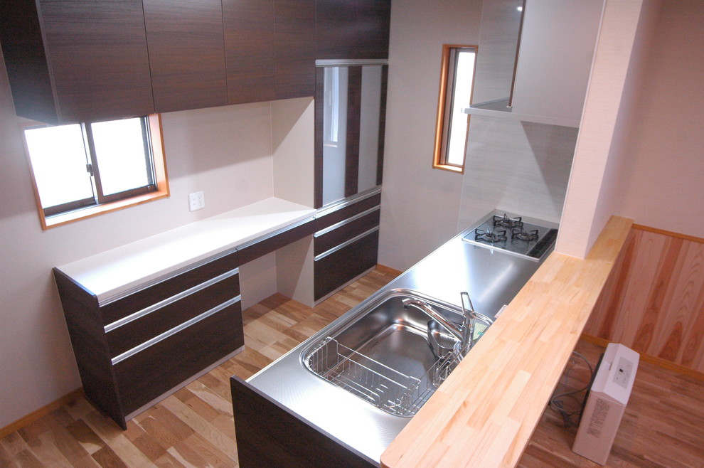 Mid-sized asian single-wall open plan kitchen in Nagoya with an integrated sink, flat-panel cabinets, dark wood cabinets, stainless steel benchtops, white splashback, stainless steel appliances, light hardwood floors, with island, beige floor and beige benchtop.