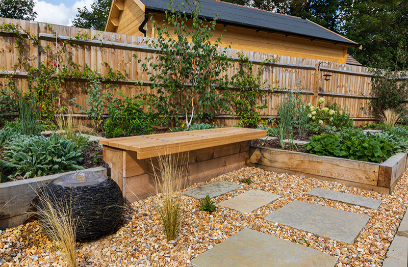 Kleiner Country Garten im Sommer, hinter dem Haus mit Hochbeet, direkter Sonneneinstrahlung, Natursteinplatten und Holzzaun in Surrey
