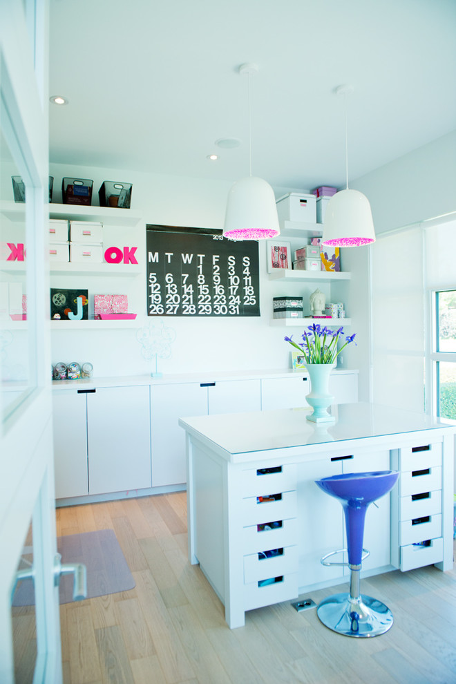 Inspiration for a contemporary craft room in Calgary with white walls, light hardwood floors and a freestanding desk.