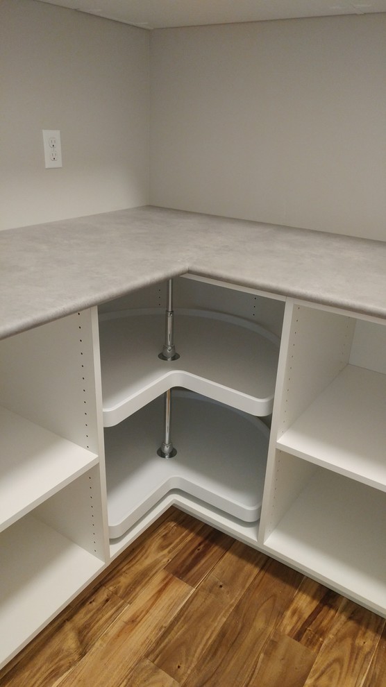 This is an example of a small modern l-shaped kitchen pantry in Milwaukee with open cabinets, white cabinets, medium hardwood floors, no island and brown floor.