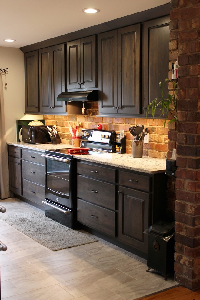 Photo of a mid-sized country galley separate kitchen in Chicago with an undermount sink, raised-panel cabinets, grey cabinets, quartz benchtops, multi-coloured splashback, brick splashback, black appliances, vinyl floors and no island.