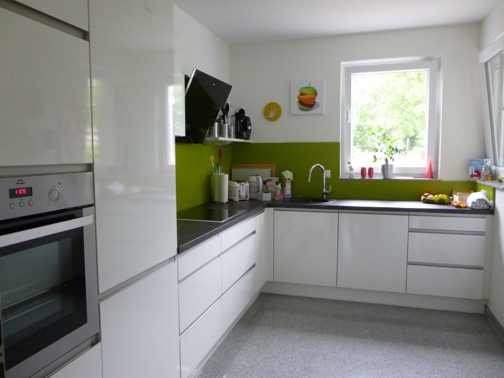 Offene Moderne Küche in L-Form mit flächenbündigen Schrankfronten, weißen Schränken und Küchenrückwand in Grün in Frankfurt am Main