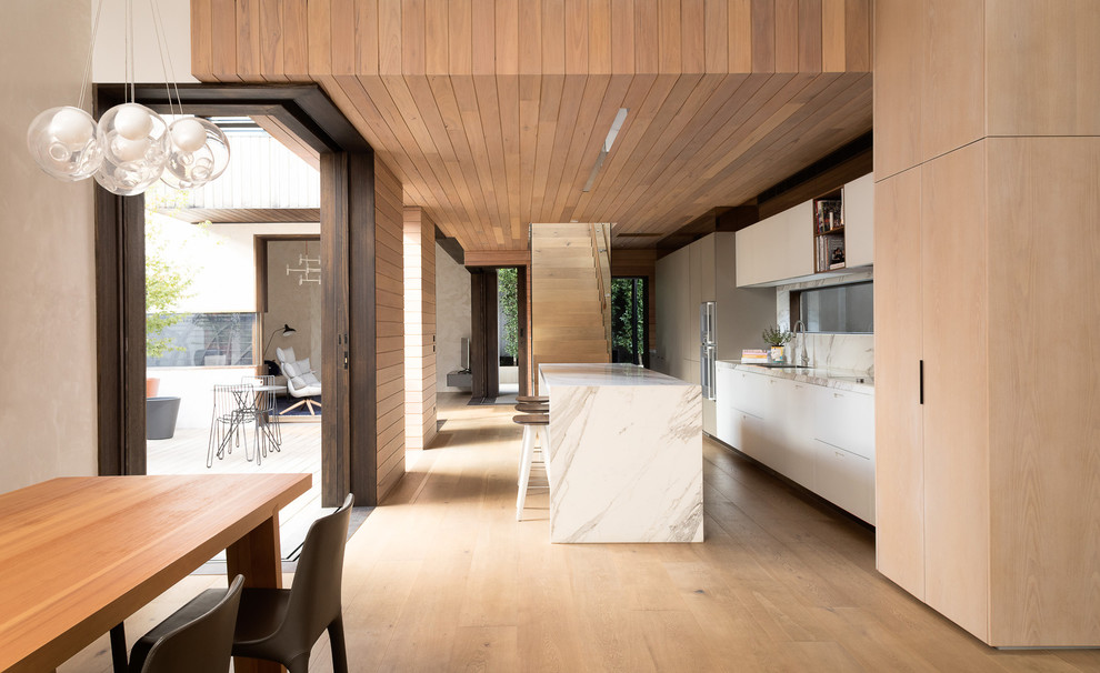 This is an example of a contemporary galley kitchen in Melbourne with an undermount sink, flat-panel cabinets, white cabinets, light hardwood floors, with island, beige floor and white benchtop.