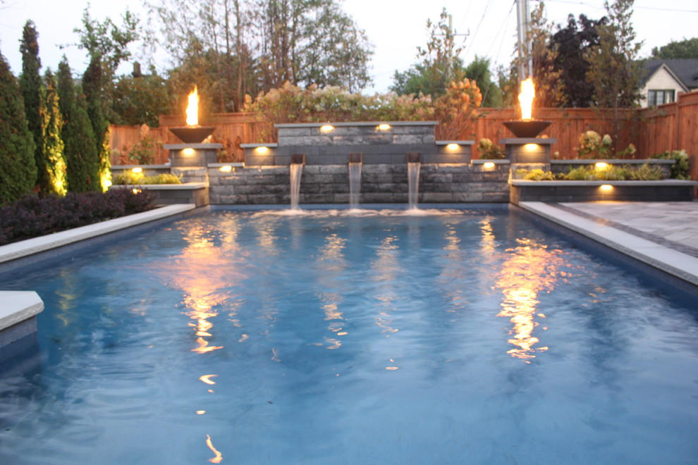 This is an example of a mid-sized modern backyard rectangular natural pool in Toronto with a water feature and concrete pavers.