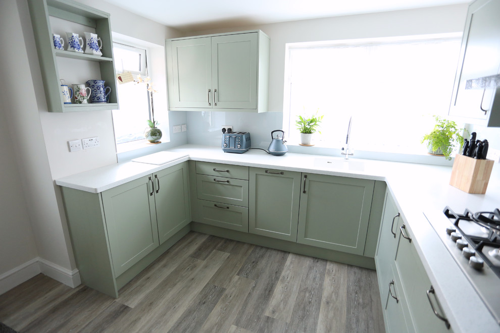Mid-sized transitional u-shaped separate kitchen in Other with an integrated sink, shaker cabinets, green cabinets, solid surface benchtops, white splashback, glass sheet splashback, black appliances, vinyl floors, no island, brown floor and white benchtop.