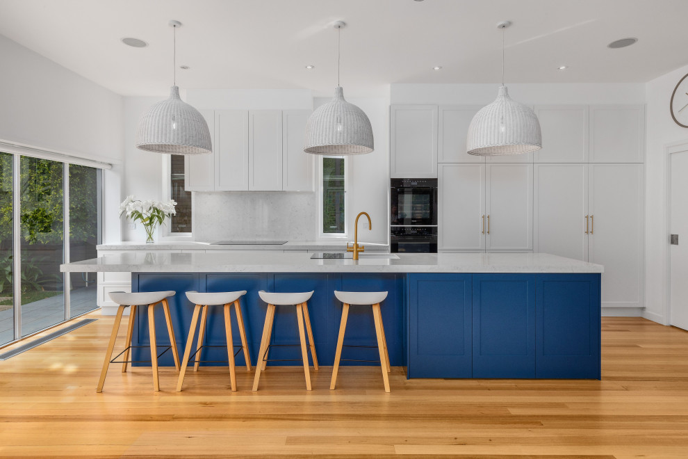 Example of a large galley medium tone wood floor eat-in kitchen design in Melbourne with an undermount sink, shaker cabinets, blue cabinets, quartz countertops, quartz backsplash, black appliances, an island and white countertops
