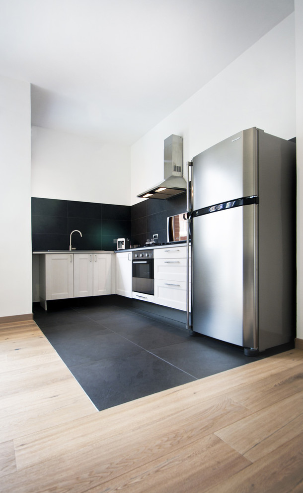 Photo of a contemporary l-shaped kitchen in Turin with recessed-panel cabinets, white cabinets, black splashback, stone slab splashback, stainless steel appliances and slate floors.