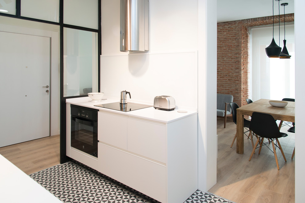 This is an example of a small modern single-wall separate kitchen in Madrid with an undermount sink, flat-panel cabinets, white cabinets, quartz benchtops, white splashback, window splashback, black appliances, ceramic floors, no island and multi-coloured floor.